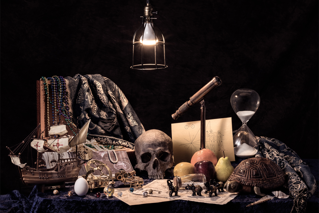 ﻿Ship, hourglass, skull, fruit, and turtle arranged on desk with light overhead